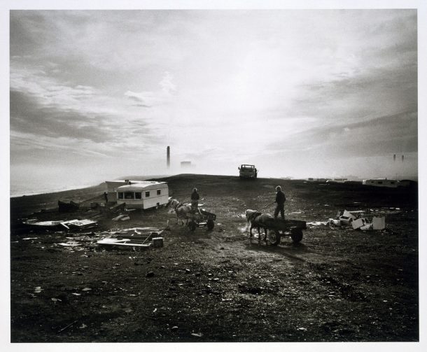 黑白照片，男人捡起石头，马和马车在平静的卵石海滩的水