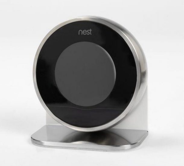 Nest Lab的学习恒温器，圆形恒温器，银色外壳，黑屏。恒温器安装在一个有圆形底座的支架上。