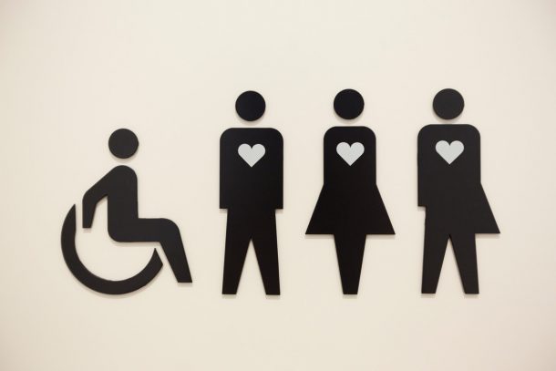 厕所门上的一个标志显示四个人排成一行，一个坐在轮椅上，另外三个人胸前有心形符号。