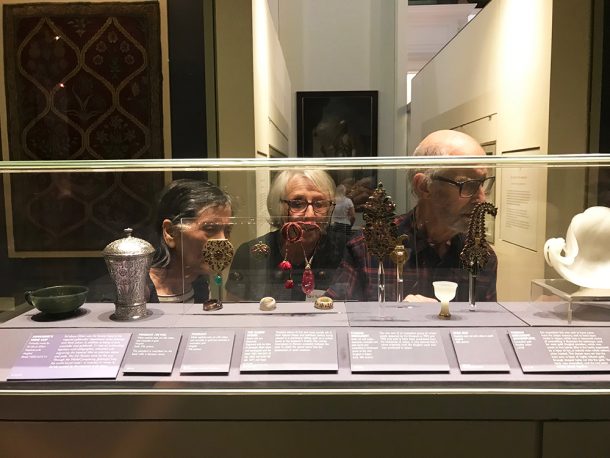 画廊里，三个人透过玻璃柜观看各种各样的物品