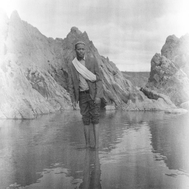 一个年轻人站在水在一个多山的背景下